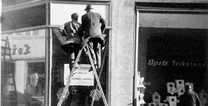 Zwei Männer stehen auf einer Leiter und befesstigen Glas an einer Fassade in einer historischen Fotografie