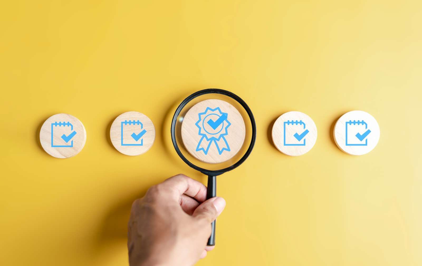 Hand hält eine Lupe vor einem Holzobjekt mit einem Siegelstempel